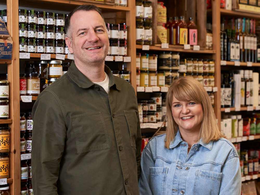 A couple standing in front of a shelf full of colourful deli items.