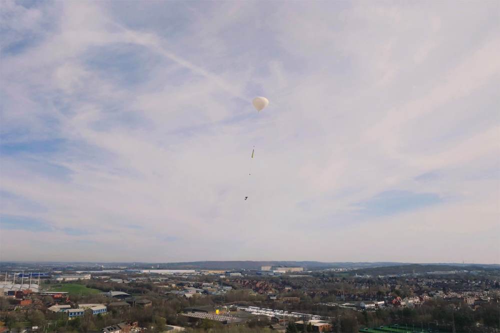 The launch rig floats above the countryside, lifted by a hydrogen balloon.